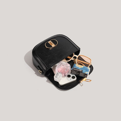 Black handbag with sunglasses, phone, and other items on a light gray background