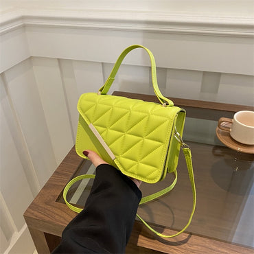 Person holding a bright green quilted handbag on a wooden surface with a blurred background