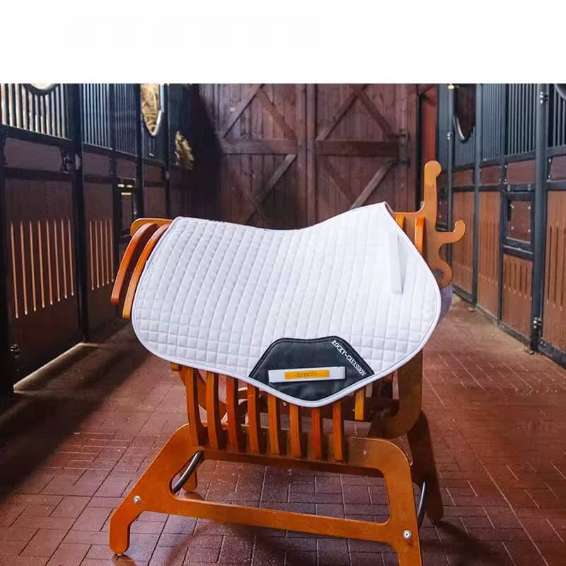 Saddle with a white quilted pad on an orange saddle stand in a stable setting