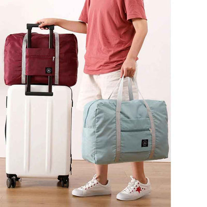 Foldable travel duffel bags in blue and red with dual carry handles, front zip pockets, and a trolley sleeve that fits over a suitcase handle for convenient travel.